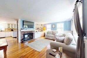 Una sala de estar con chimenea, un sofá, un televisor y una cocina con armarios y mostrador.