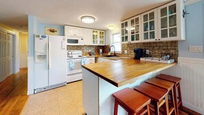 Eine Küche mit weißen Schränken, einer Holzausziehtafel und einer eingebauten Kochinsel mit Hockern.