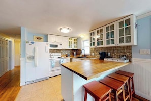 Una cocina con armarios blancos, encimera de madera y una isla integrada con taburetes.
