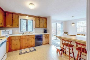 A kitchen with wooden cabinets, a dishwasher, a microwave, and a bar area with stools. - Friendly retreat with a deck, AC, and board games - stellar central location (Chatham)