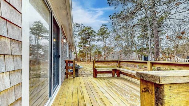 Eine Holzterrasse mit einer Bank, einer Glastür und Blick auf Bäume.