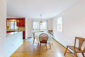 A room with a dining table, chairs, a window with curtains, a wooden bench, and a kitchen area with red cabinets and a hanging light fixture. - Friendly retreat with a deck, AC, and board games - stellar central location (Chatham)