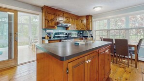 Een keuken met houten kastjes, een centraal eiland en een eethoek met stoelen.