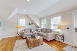 A living room with a high ceiling, two sofas, a coffee table, and two lamps. - New Lavish Condo in Heart of Downtown Chatham - Walk to Dining, Shops & Beach (Chatham)