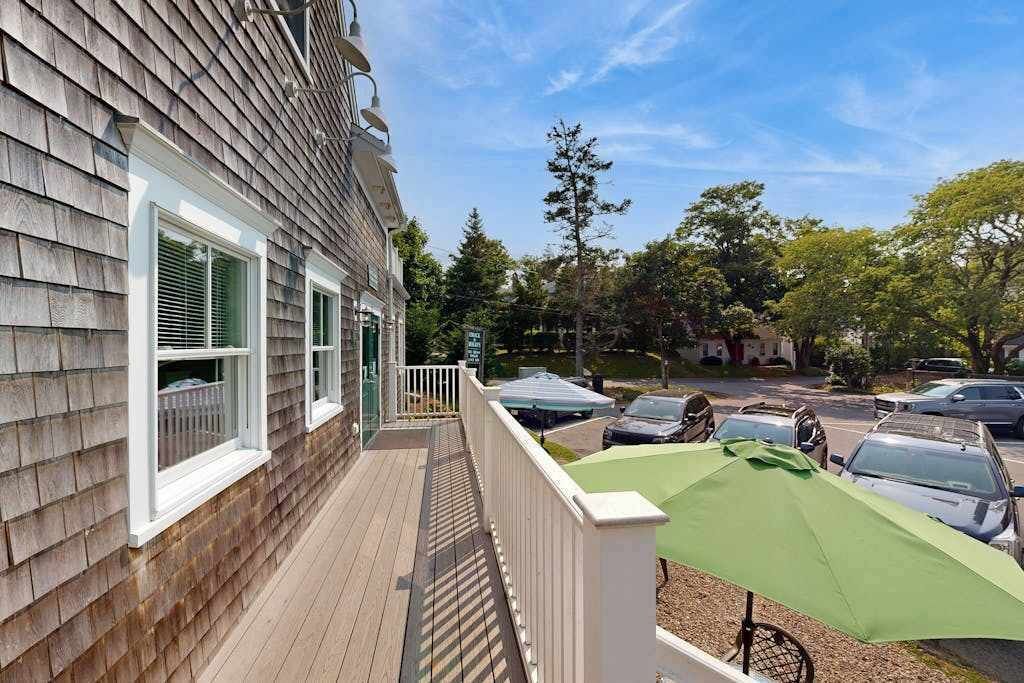 En boligbygning med træfacade, overdækket veranda og en grøn parasol.