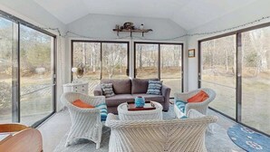 Une pièce spacieuse avec de grandes fenêtres, un canapé, des fauteuils en osier et une petite table.