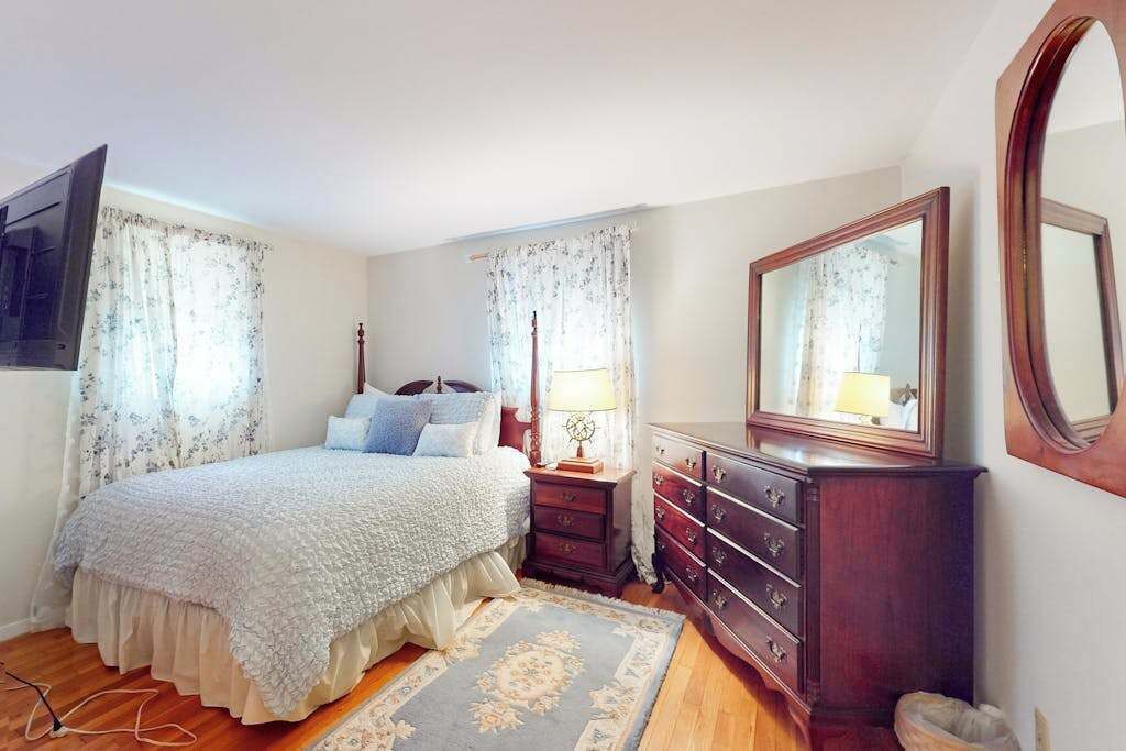 Een slaapkamer met een bed, een dressoir, een spiegel en gordijnen.