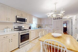 A kitchen with white cabinets, a wooden dining table, and a chandelier. - Traditional coastal home with large yard, gazebo, grill, smart TVs, washer/dryer (Centerville)