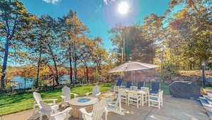 Eine Terrasse im Freien mit Adirondack-Stühlen, einem runden Tisch und einem Grillbereich.
