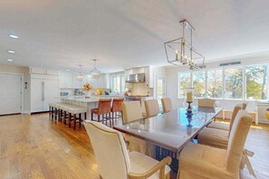 A spacious kitchen with a large island, white cabinetry, and a dining area with a glass-top table and chairs. - Sprawling dog-friendly lake estate with pool, patio, fire pit, games, & views (Barnstable)