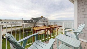 En balkon med havudsigt, et træbord og to Adirondack-stole.