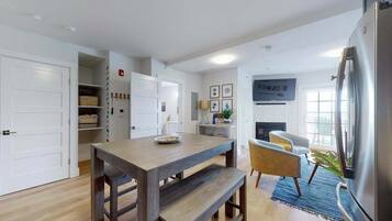 A modern kitchen with a wooden table, a refrigerator, and a dining area with chairs.