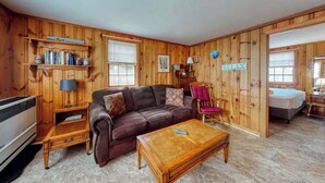 A cozy room with a brown leather couch, a wooden coffee table, a bookshelf, a chair, and a bed. - Family-friendly house w/gas grill, deck, streaming services - near Haigis Beach (Dennis Port)