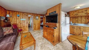 A wooden interior with a sofa, coffee table, TV, and kitchen area. - Family-friendly house w/gas grill, deck, streaming services - near Haigis Beach (Dennis Port)