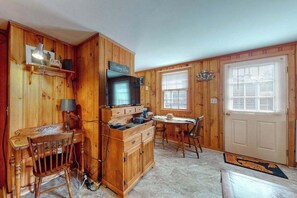 Interior de una cabaña de madera con cocina, comedor y una puerta con ventana.