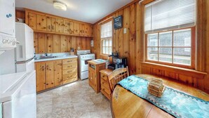 A kitchen with wooden cabinets, a stove, a sink, and a dining area with a table and chairs. - Family-friendly house w/gas grill, deck, streaming services - near Haigis Beach (Dennis Port)