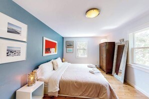 Un dormitorio con cama, mesitas de noche, armario y cuadros en la pared.