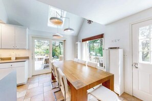 A modern kitchen with a large wooden table, white cabinets, and a view of the outdoors. - Spacious Dennis Home with Large Deck & Backyard - Walk to Corporation Beach (Dennis)
