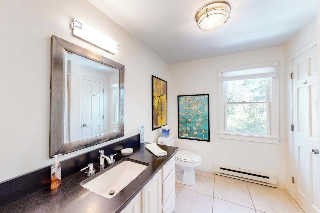 Une salle de bain avec un grand miroir, un lavabo, des toilettes et une fenêtre.
