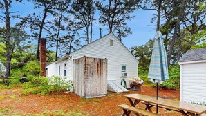 A rustic wooden shed, a picnic table, and a striped umbrella in a wooded backyard.