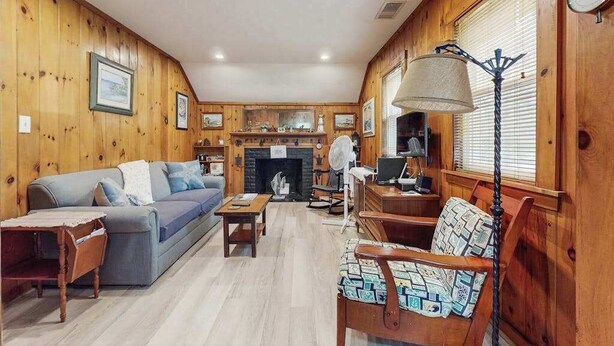 A wooden-paneled room with a sofa, chairs, a table, a fireplace, and a clock.