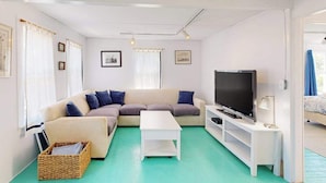 Ein Wohnzimmer mit einer Couch, einem Fernseher, einem weißen Couchtisch und einem Korbwäschesammler.
