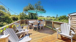 Eine Holzterrasse mit Adirondack-Stühlen, einem Tisch und einem Sonnenschirm.
