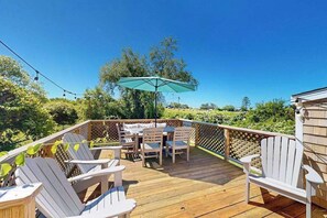 A wooden deck with Adirondack chairs, a table, and an umbrella. - Water-view home in great location with spacious backyard, grill, kayaks, dogs OK (Chilmark)