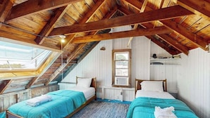 Ein Zimmer mit zwei Betten, Holzbalken, einem Oberlicht und einem Fenster.