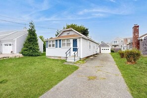 A single-story house with a front porch, a small staircase, and a driveway leading to the garage. - Cozy home close to the beach with patio, Washer/Dryer, & Partial AC (Barnstable)