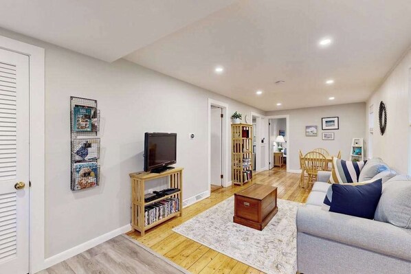 A living room with a television, bookshelf, and a sofa. - Cozy home close to the beach with patio, Washer/Dryer, & Partial AC (Barnstable)