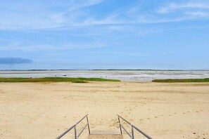 A beach with a staircase leading to a sandy area, a clear sky, and a calm sea. - Cozy home close to the beach with patio, Washer/Dryer, & Partial AC (Barnstable)