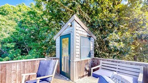 Een houten terras met een tuinhuisje, twee blauwe fauteuils en een bank.