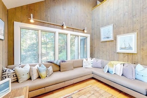 Ein gemütliches Zimmer mit großem Fenster, einer Holzwand und einer Couch mit vielen Kissen.