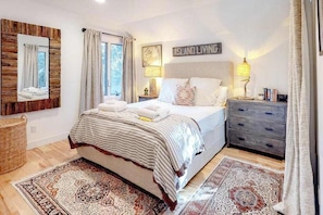 Ein Schlafzimmer mit einem Bett, zwei Nachttischlampen, einem Nachttisch, einer Kommode, einem Spiegel und einem Teppich.