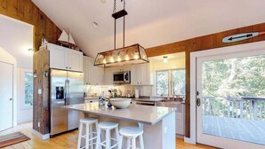 Een moderne keuken met een centraal kookeiland, barstoelen, houten lambrisering en een grote schuifpui naar buiten.
