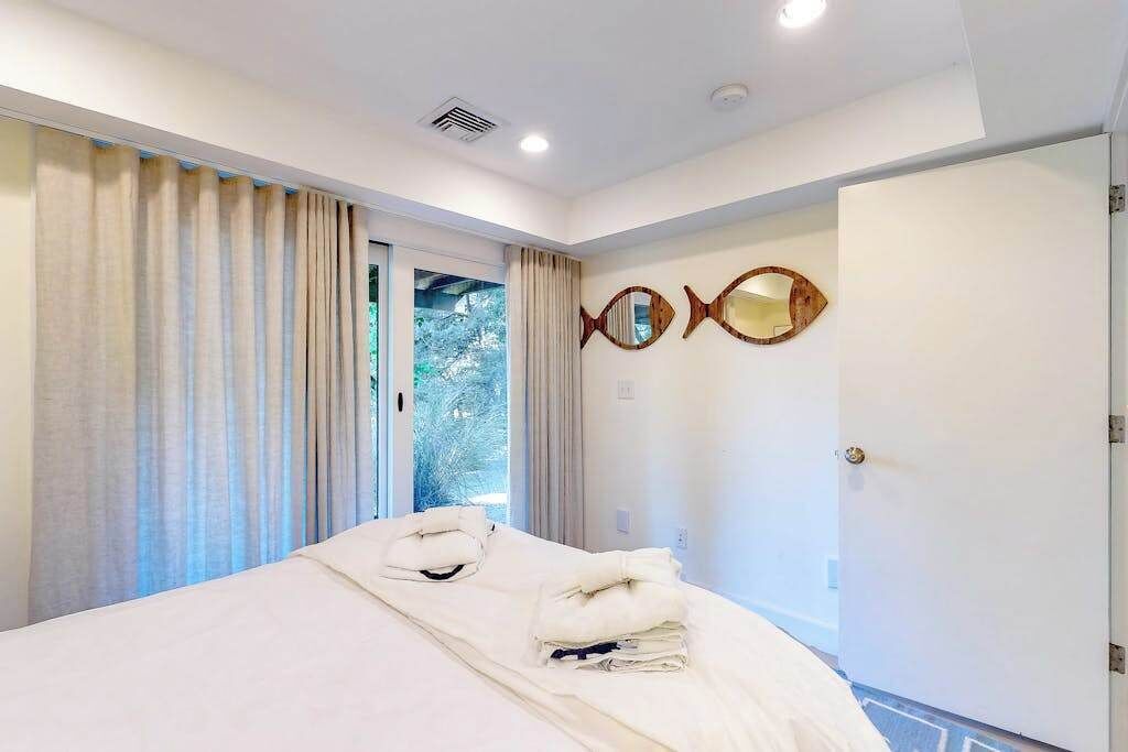 Een hotelkamer met een bed, gordijnen, een deur en een spiegel in de vorm van een vis, bevestigd aan de muur.