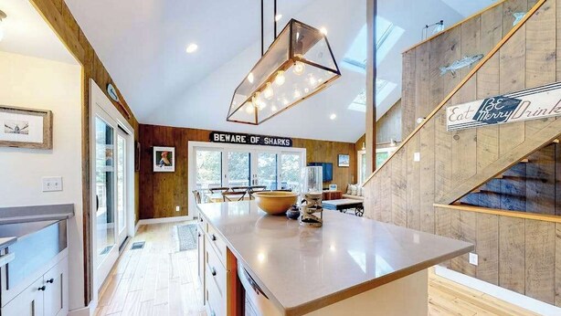 Een moderne keuken met een houten kookeiland, een bord met de tekst 'BEWARE OF SHARKS' en een trap met een bord waarop staat 'Eat Merry Drink'.