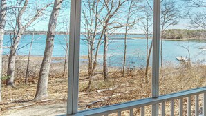 Une vue à travers une fenêtre donnant sur une terrasse en bois, des arbres et une étendue d’eau.