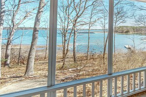 Blick durch ein Fenster auf ein Holzdeck, Bäume und ein Gewässer.