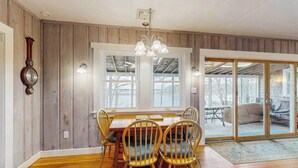 Un espace repas comprenant une table et des chaises en bois, de grandes fenêtres et une porte-fenêtre coulissante donnant sur un espace extérieur.