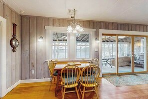 Ein Essbereich mit Holztisch und Stühlen, großen Fenstern und einer Glastür zum Außenbereich.