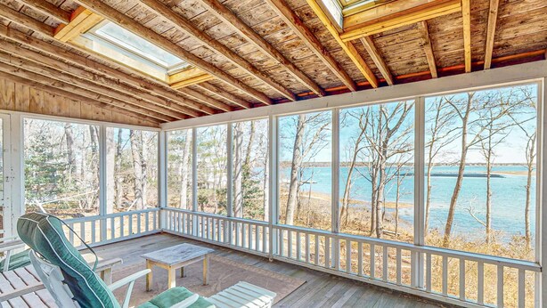 Un espace extérieur abrité, aménagé avec des sièges, et offrant une vue sur la mer et les arbres.