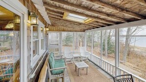 Une véranda couverte avec des poutres en bois, de grandes fenêtres et des sièges d’extérieur.