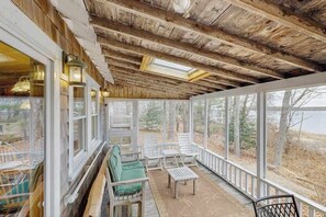 Eine Veranda mit Holzbalken, großen Fenstern und Sitzmöbeln im Freien.