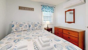 Quarto com cama, penteadeira, espelho, janela com persianas e um letreiro na parede.