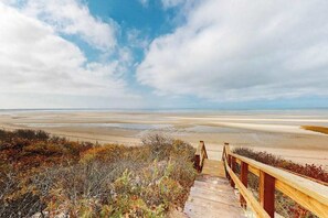 Ein hölzerner Steg führt zu einem Strand, der unter blauem Himmel liegt.