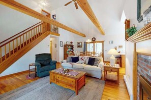 A spacious living room with a wooden staircase, a fireplace, and a cozy seating area. - Peaceful cottage with deck, screened porch, grill, & firepit - walk to beach (Eastham)