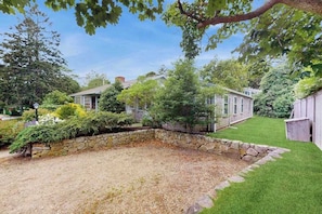 A stone wall, a grassy yard, and a house with a chimney.