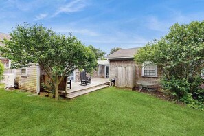A backyard with a wooden deck, a barbecue grill, and a small table.